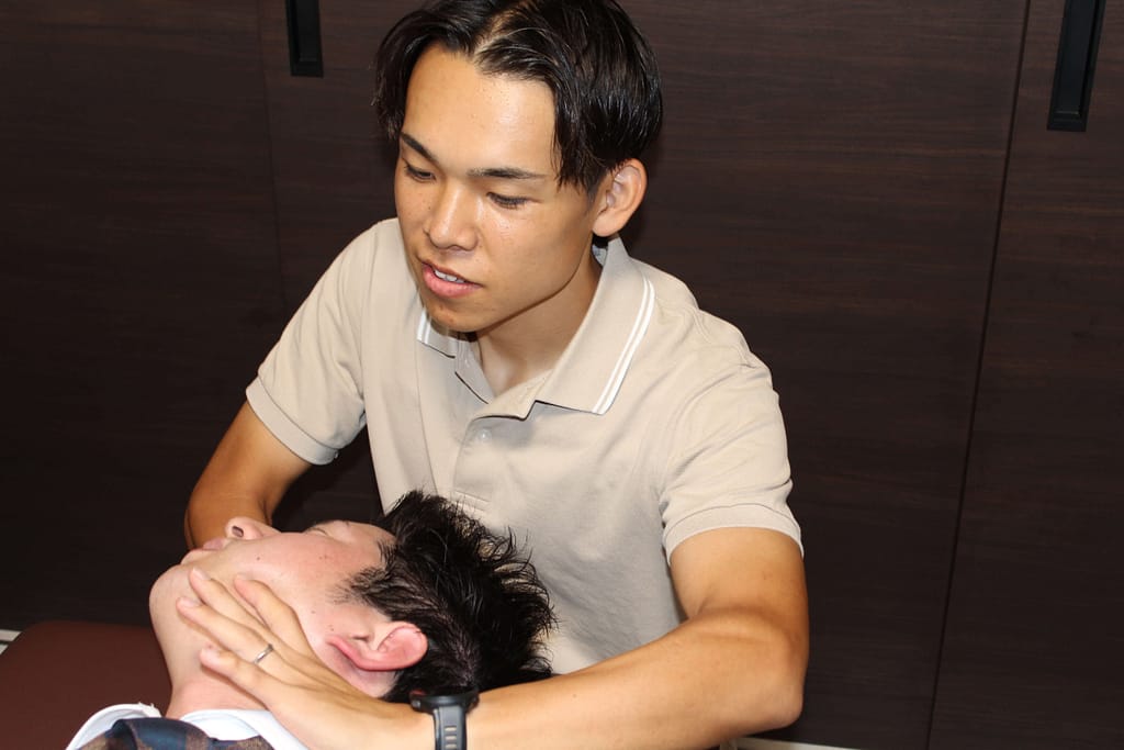院長が男性従業員の頸にカイロプラクティックを行っている写真
