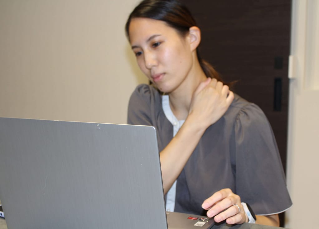 デスクワーク時に肩こりを抱え悩んでいる女性従業員