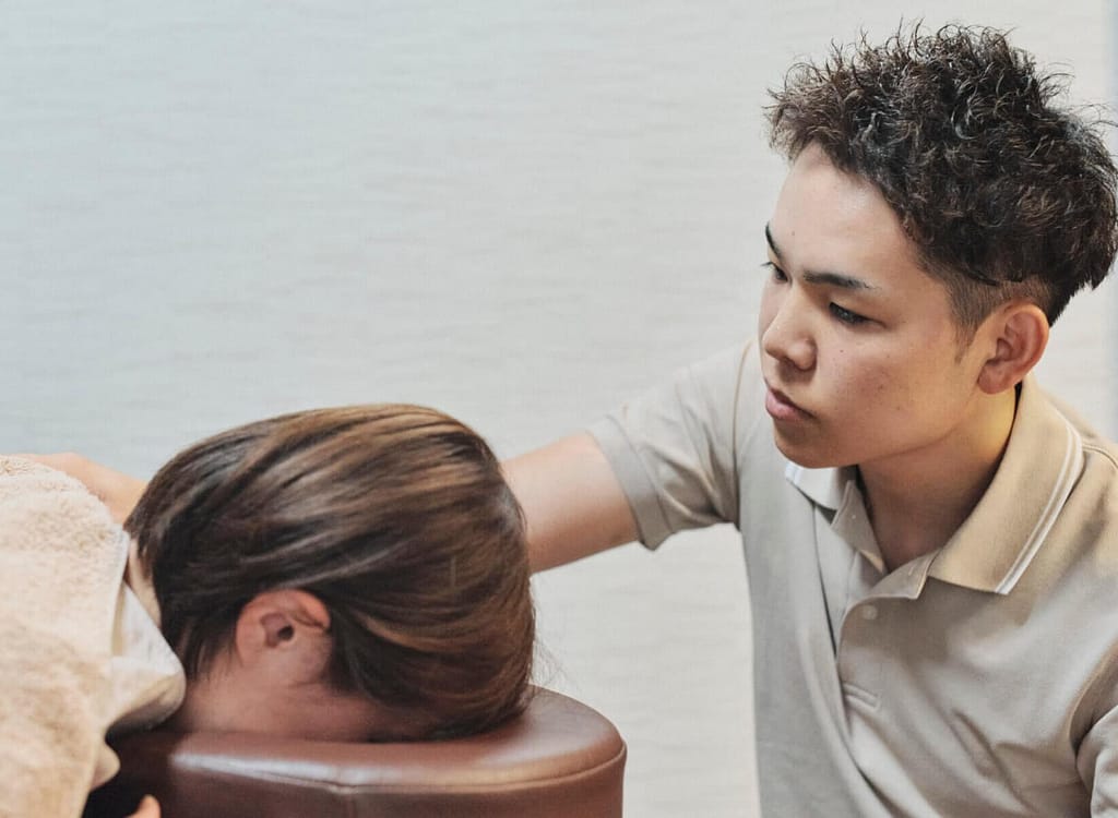 院長が企業に訪問し、うつ伏せで寝ている女性従業員の左肩を右手でマッサージしている写真