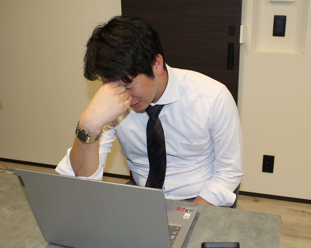 デスクワークをしている男性従業員が眼精疲労と頭痛に悩んでいる写真